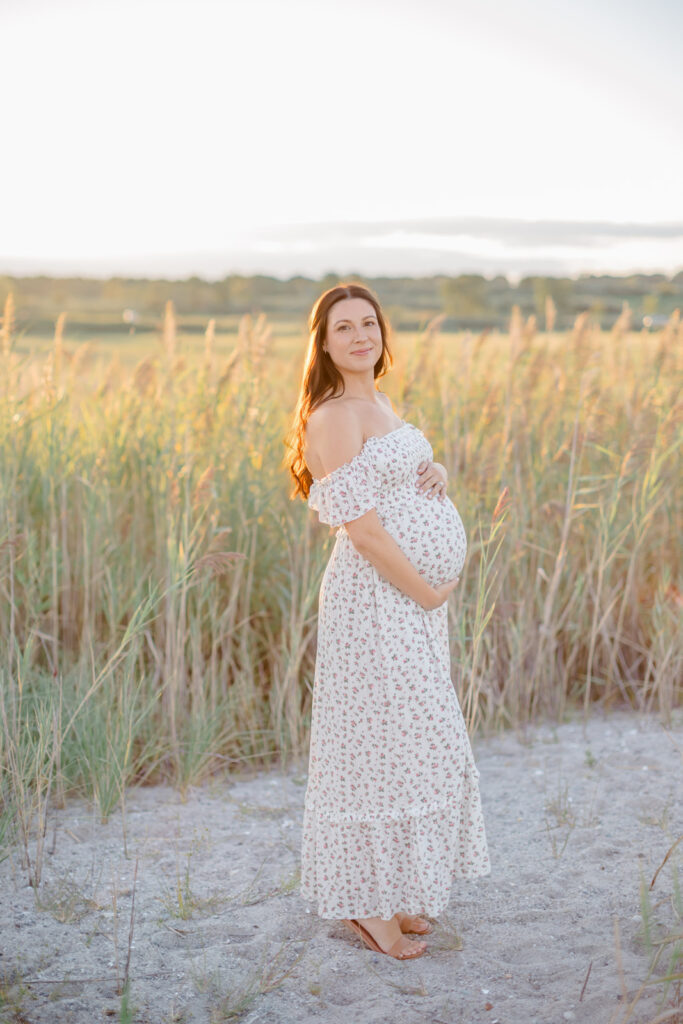 pregnant mom holding her belly while she poses on a connecticut beach