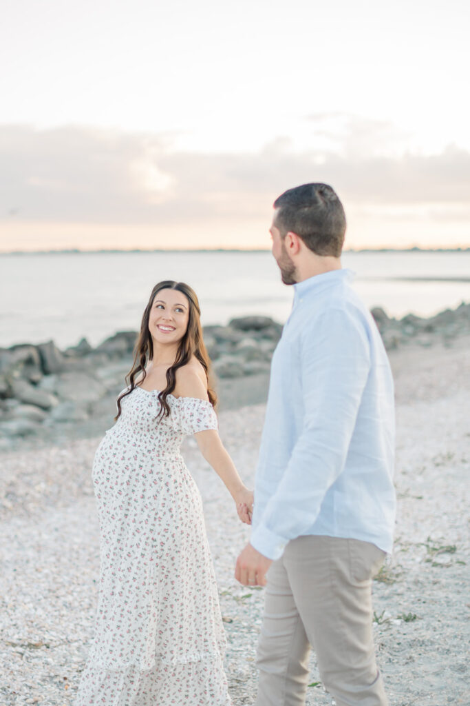 pregnant mom in a dress holding hands with husband on a connecticut beach