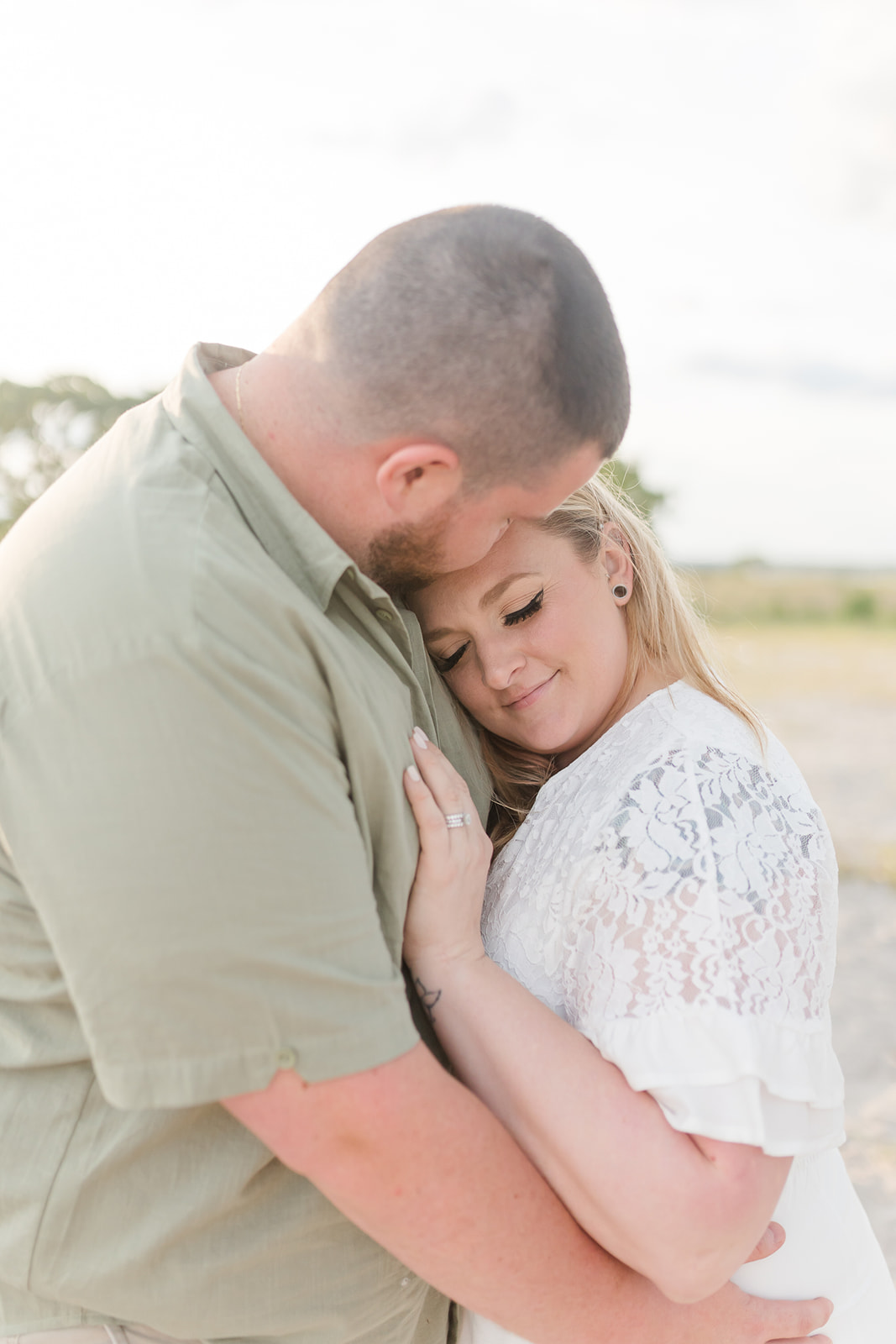 A couple snuggles while standing on a beach at sunset