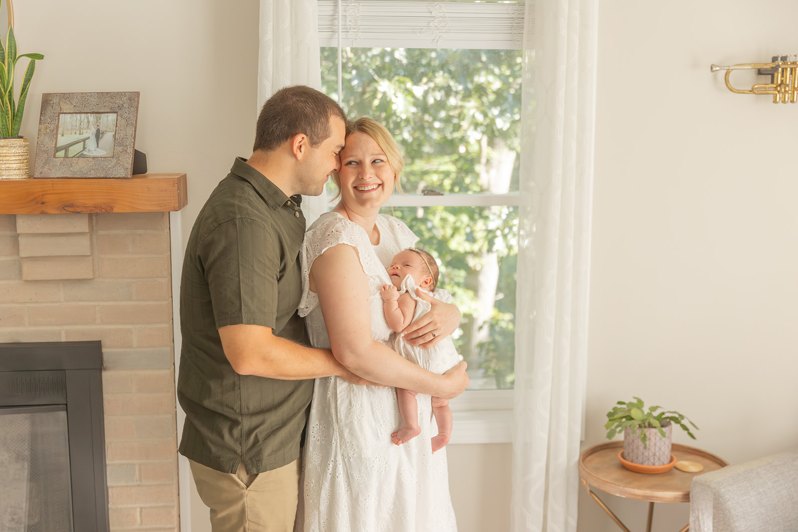 A mom and dad laugh together while holding their sleeping newborn baby against mom's chest after getting Car Seat Installation CT