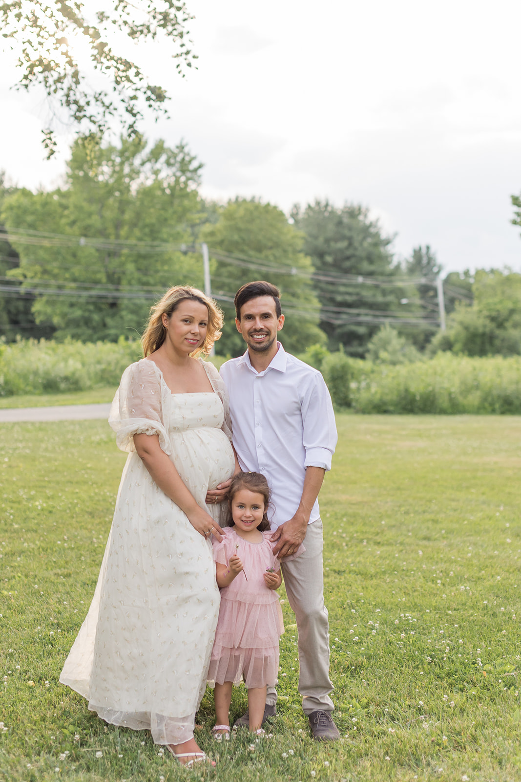 A pregnant mom stands with dad and their toddler daughter in a park field before a Home Birth CT