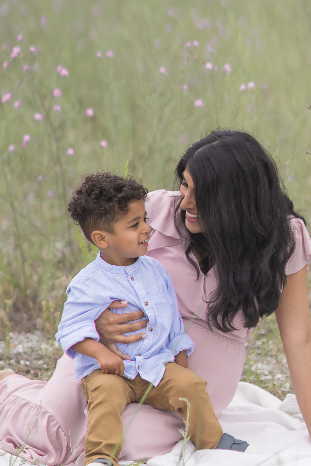 A toddler boy sits on mom's lap on a picnic blanket in a field of pink wildflowers thanks to Maternal Fetal Medicine Yale