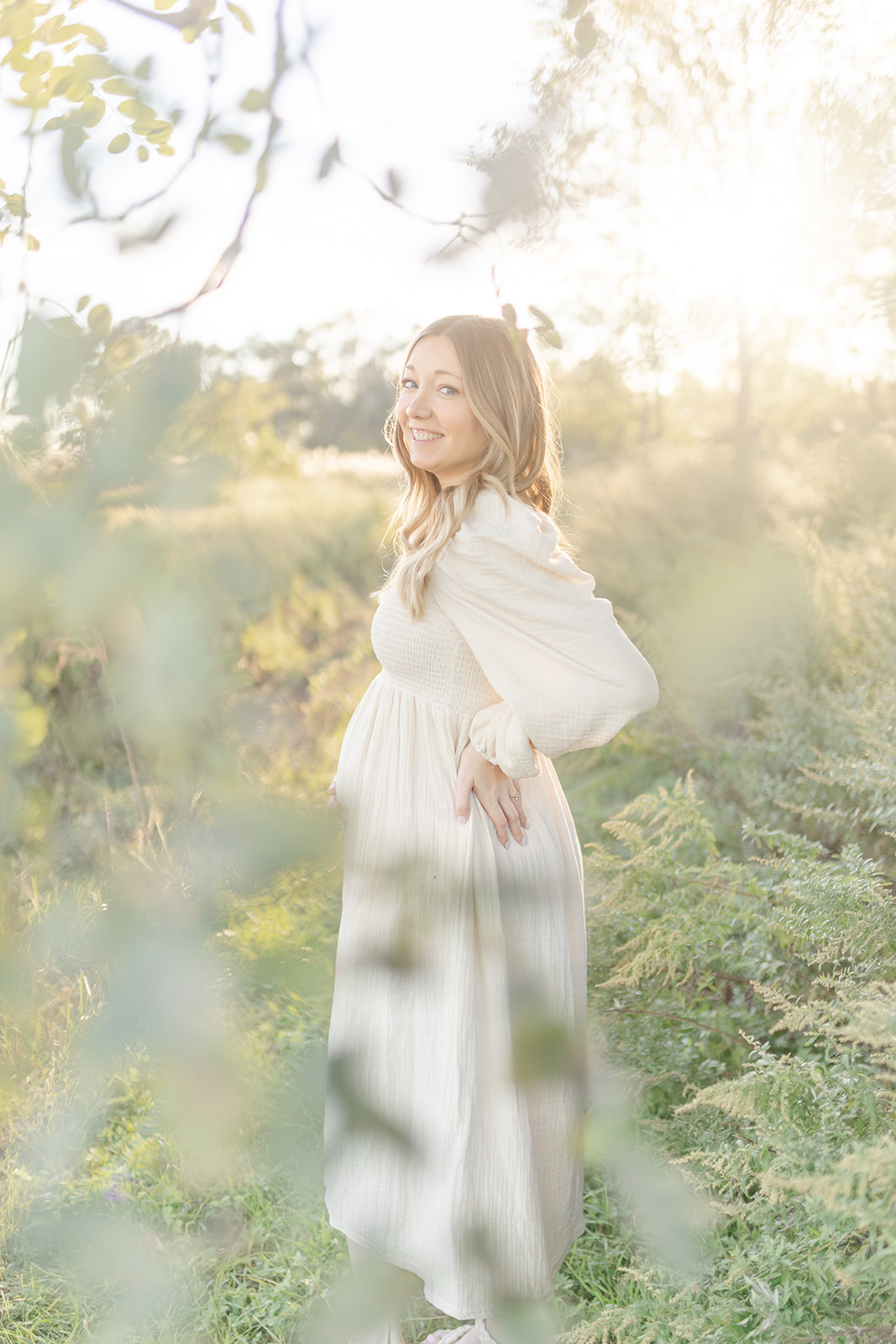 A mom to be in a white dress stands with a hand on her hip in a park at sunset after some Pelvic Floor Therapy CT
