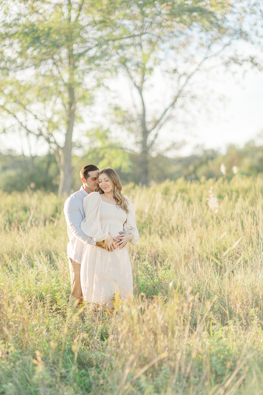 A mom to be stands in a field of tall grass nuzzling with her husband after come Pelvic Floor Therapy CT
