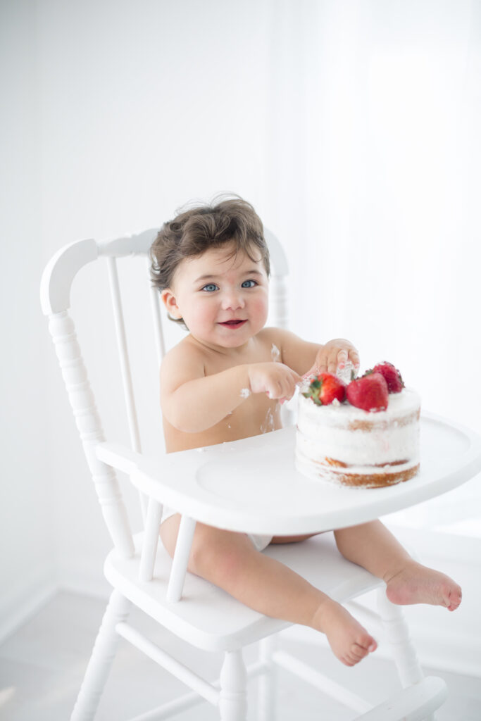 first birthday themes of strawberries on cakes of a one year old girl eating and smiling