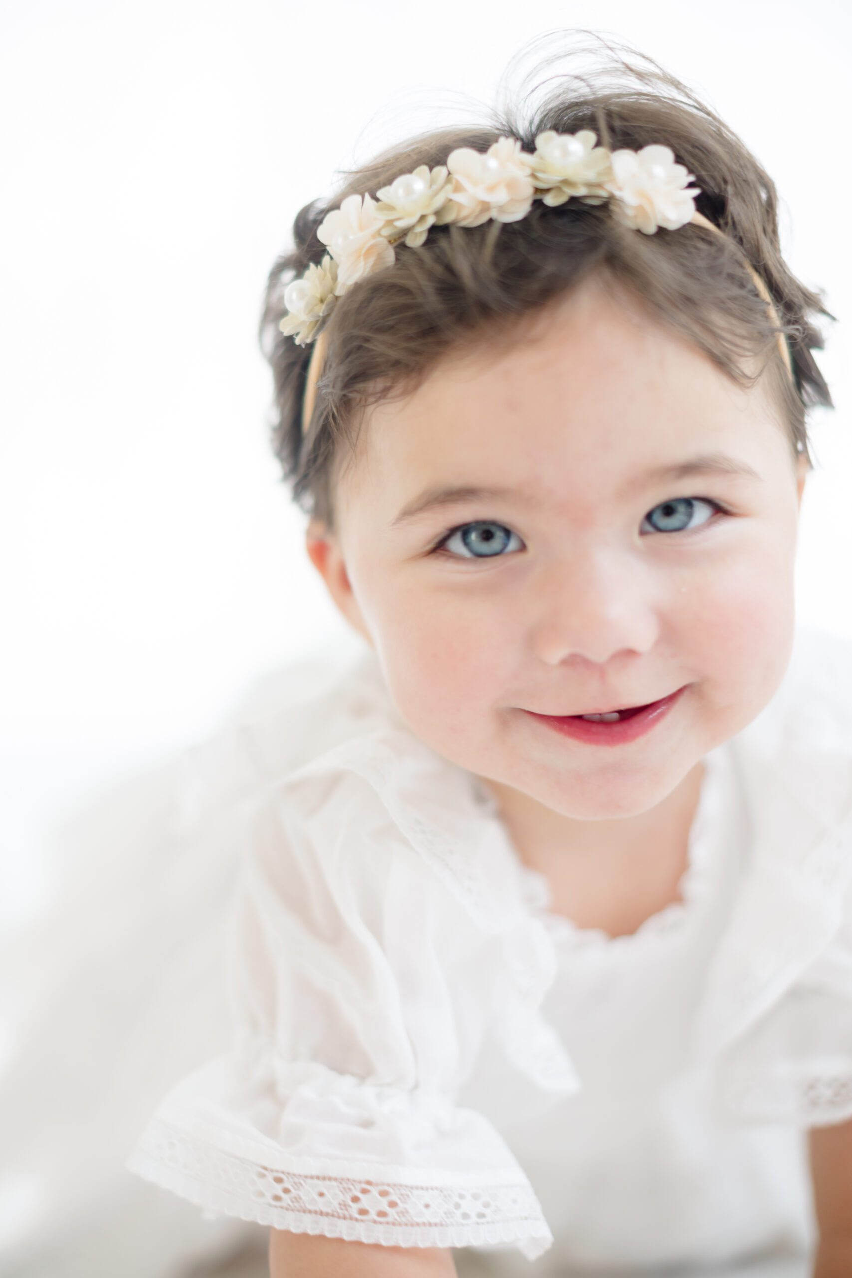 little girl dressed in a white dress with a flowered headband celebrating her first birthday