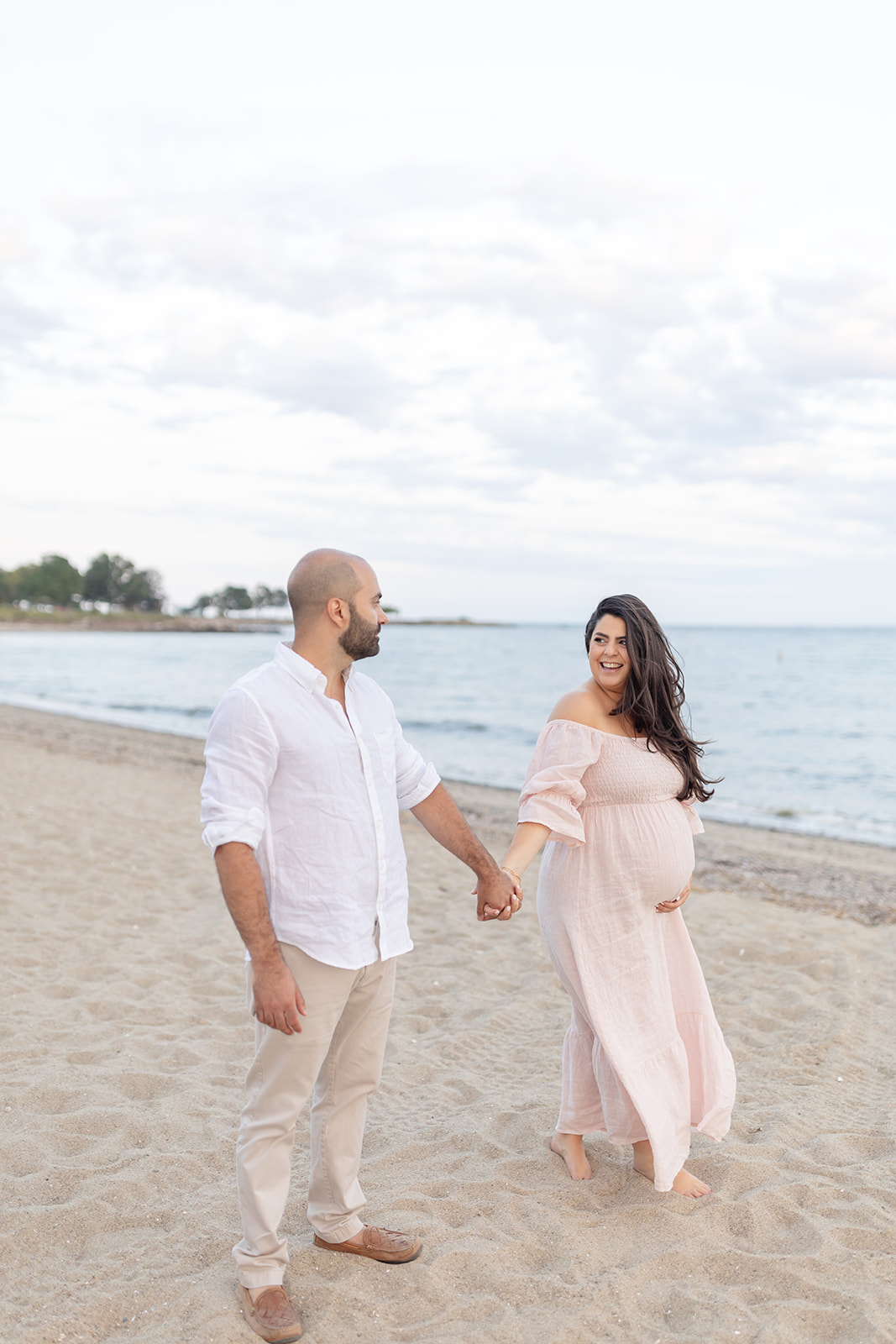 A couple holding hands, mom holding her pregnant belly in pink dress