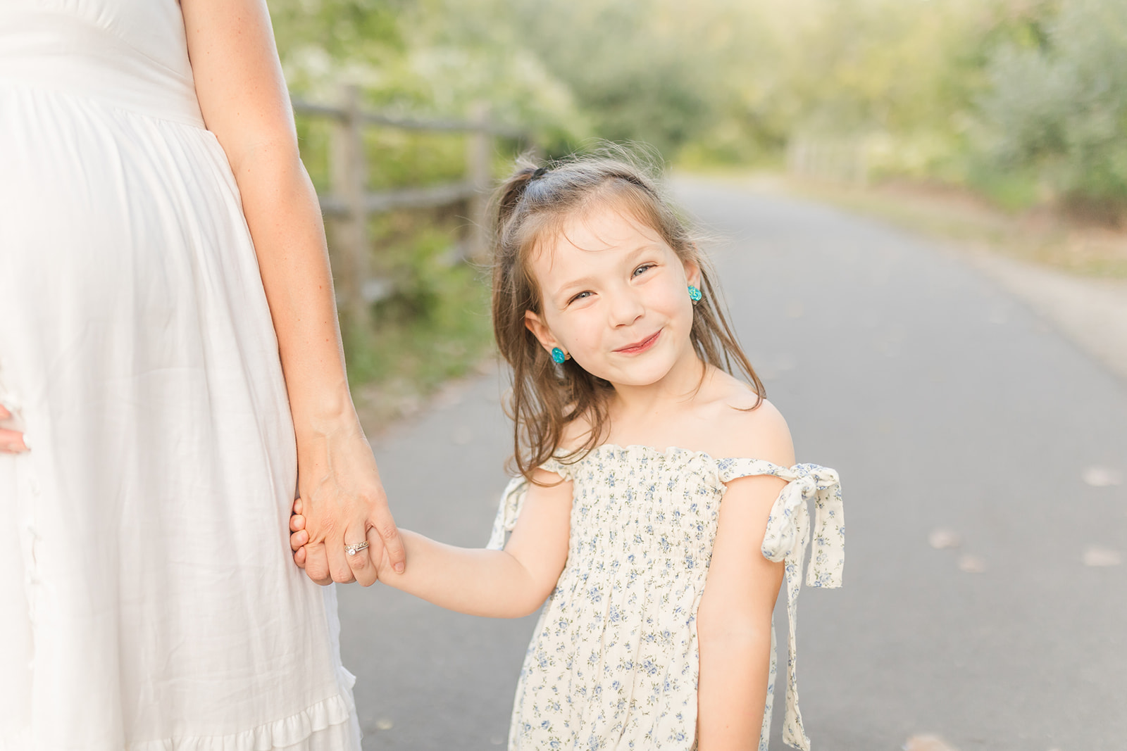 A young girl in a floral dress walks down a park path holding mom's hand after Mommy and Me Classes Fairfield CT