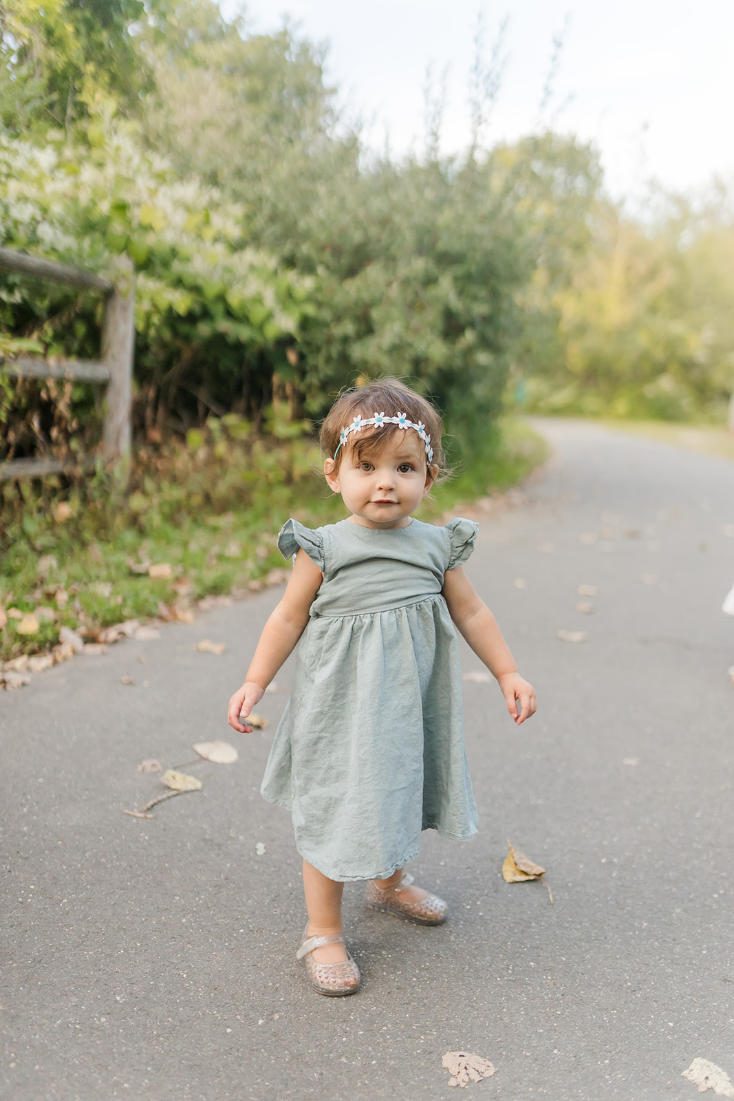 A toddler girl in a green dress stands in a park path at sunset thanks to an Au Pair Connecticut