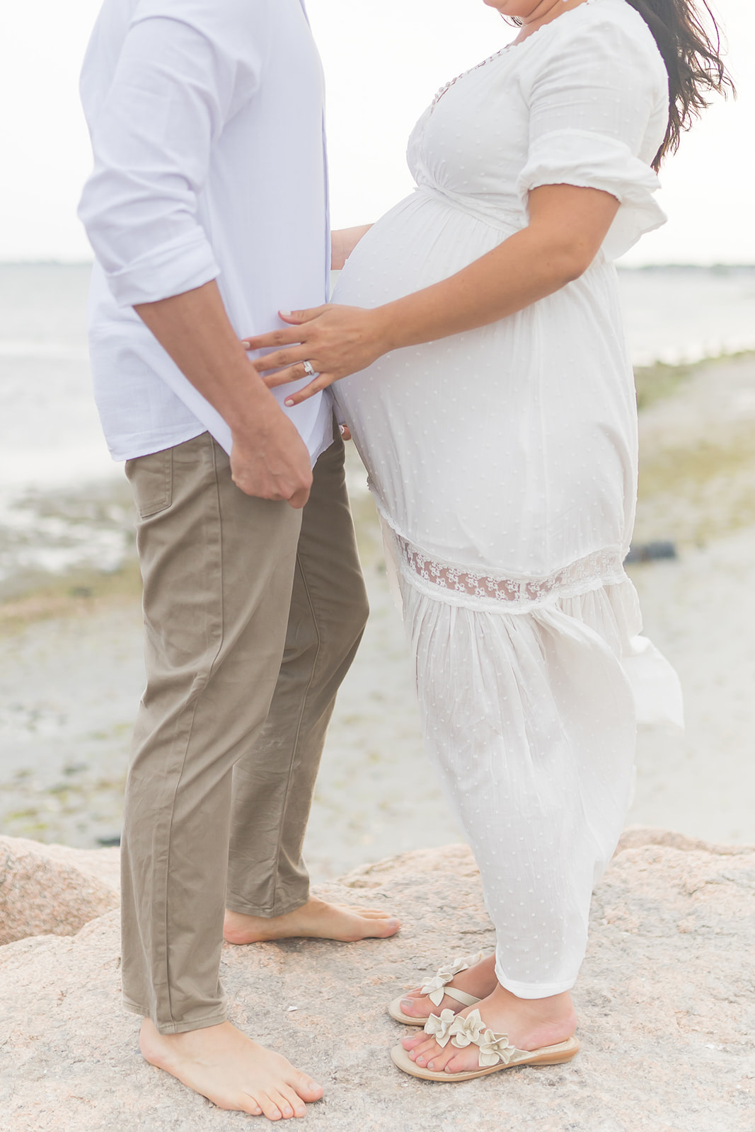 Details of a mom to be and dad standing on a windy beach