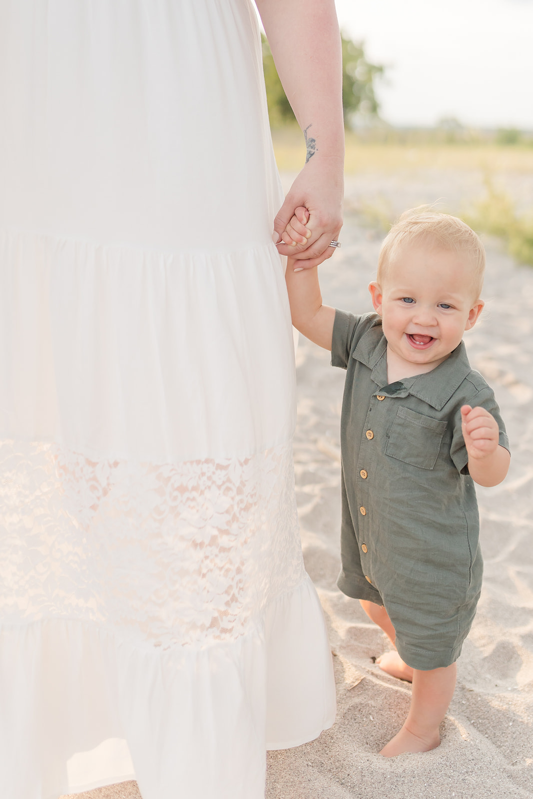 A toddler boy walks down one of the Best Connecticut Beaches For Families while holding mom's hand