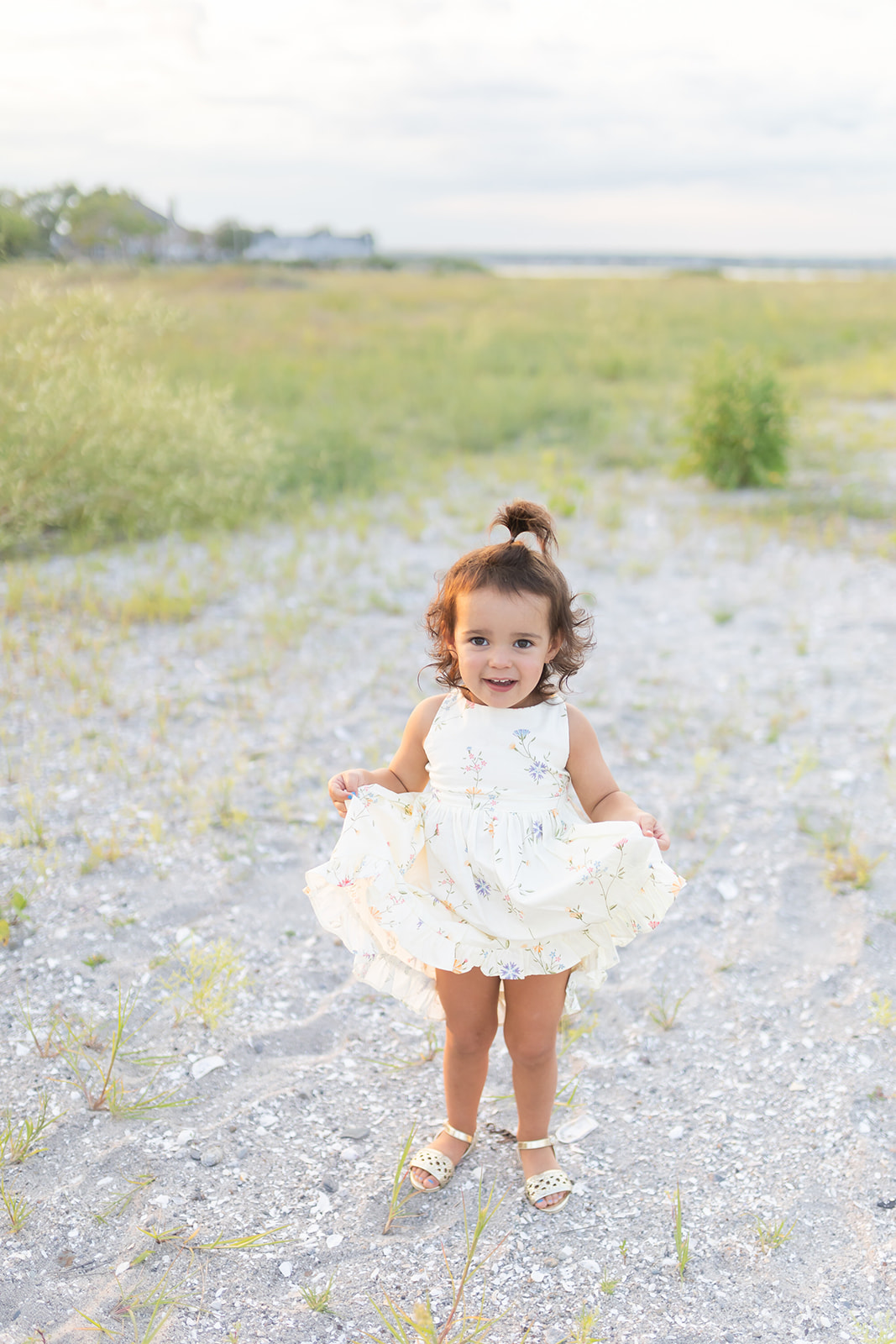 A young toddler. girl in a white dress holds it on a beach at sunset after playing at Birthday Parties Fairfield CT