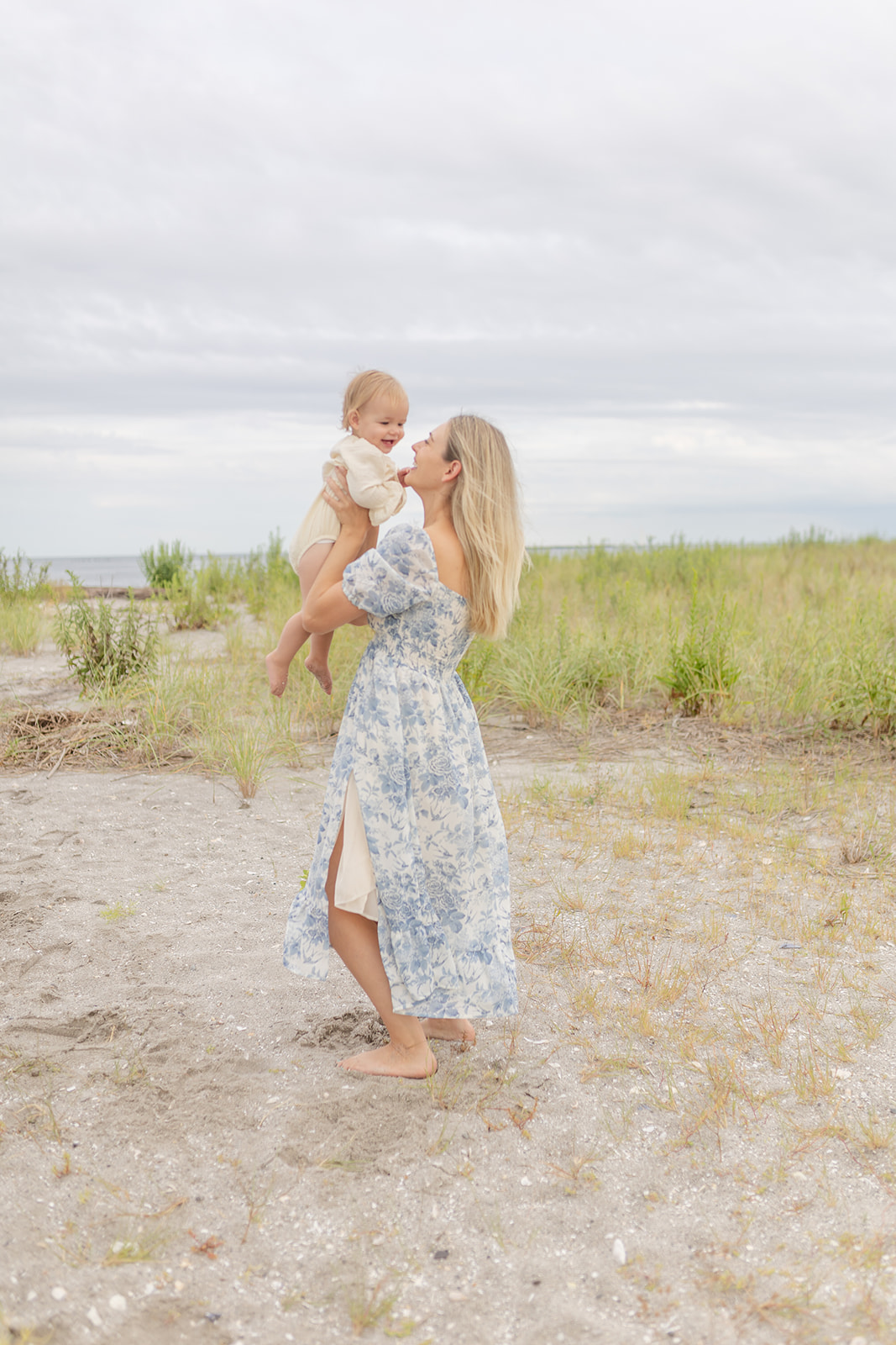 A mother in a blue dress lifts and plays with her toddler daughter on a beach before visiting Center for Pediatric Therapy Fairfield