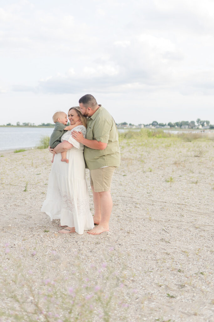 A mom and dad play and snuggle with their toddler son on a beach at sunset before visiting a Child Therapist Fairfield CT