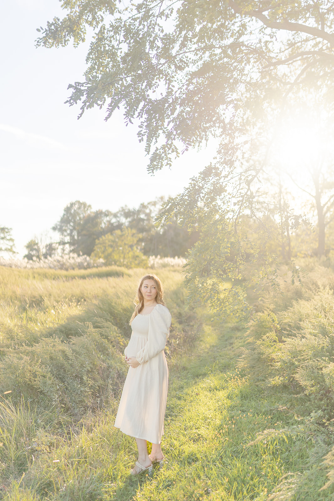 A mom to be walks through a grassy park trail at sunset while holding her bump