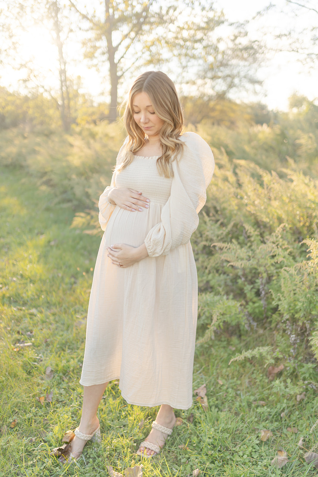 A mother to be smiles down at her bump as she walks in a park trail at sunset