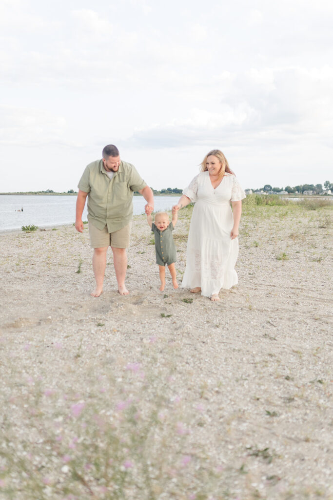 A mom and dad walk down a beach swinging their toddler son between them after visiting a Daycare Bridgeport CT