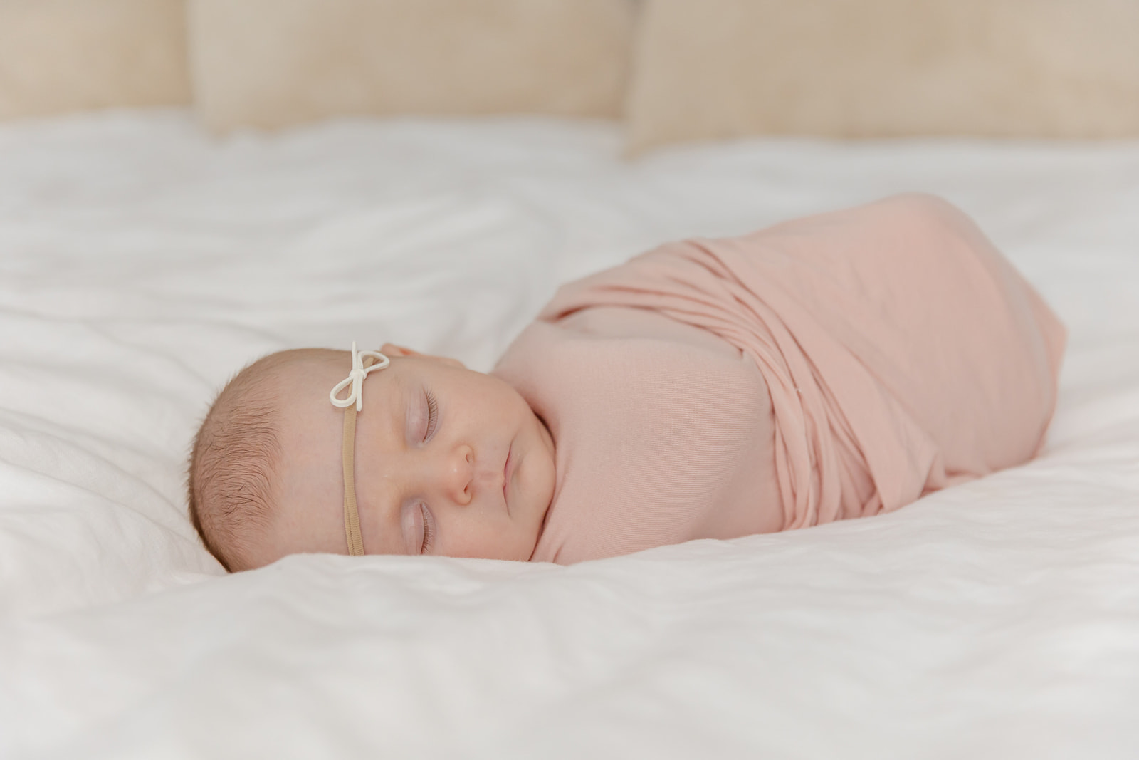 A newborn baby sleeps in a pink swaddle on a white bed in a studio before visiting a Daycare Trumbull CT