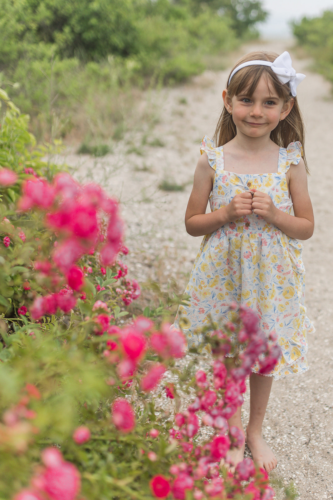 A young girl stands in a beach trail exploring pink wild flowers