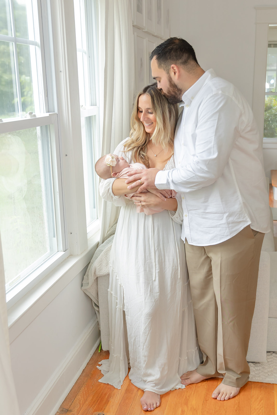 A mom and dad stand in a window smiling down at their sleeping newborn baby in mom's arms thanks to night nurse CT