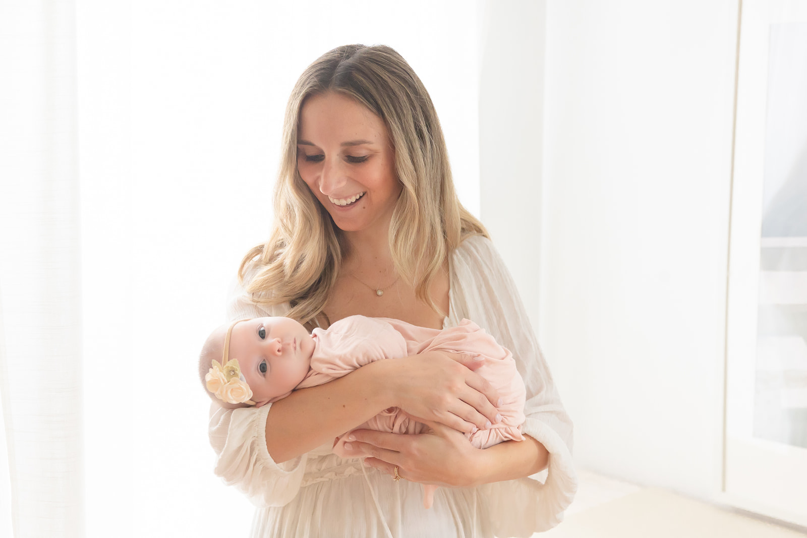 A mother laughs down at her newborn baby flopping over her arm in a pink swaddle thanks to night nurse CT