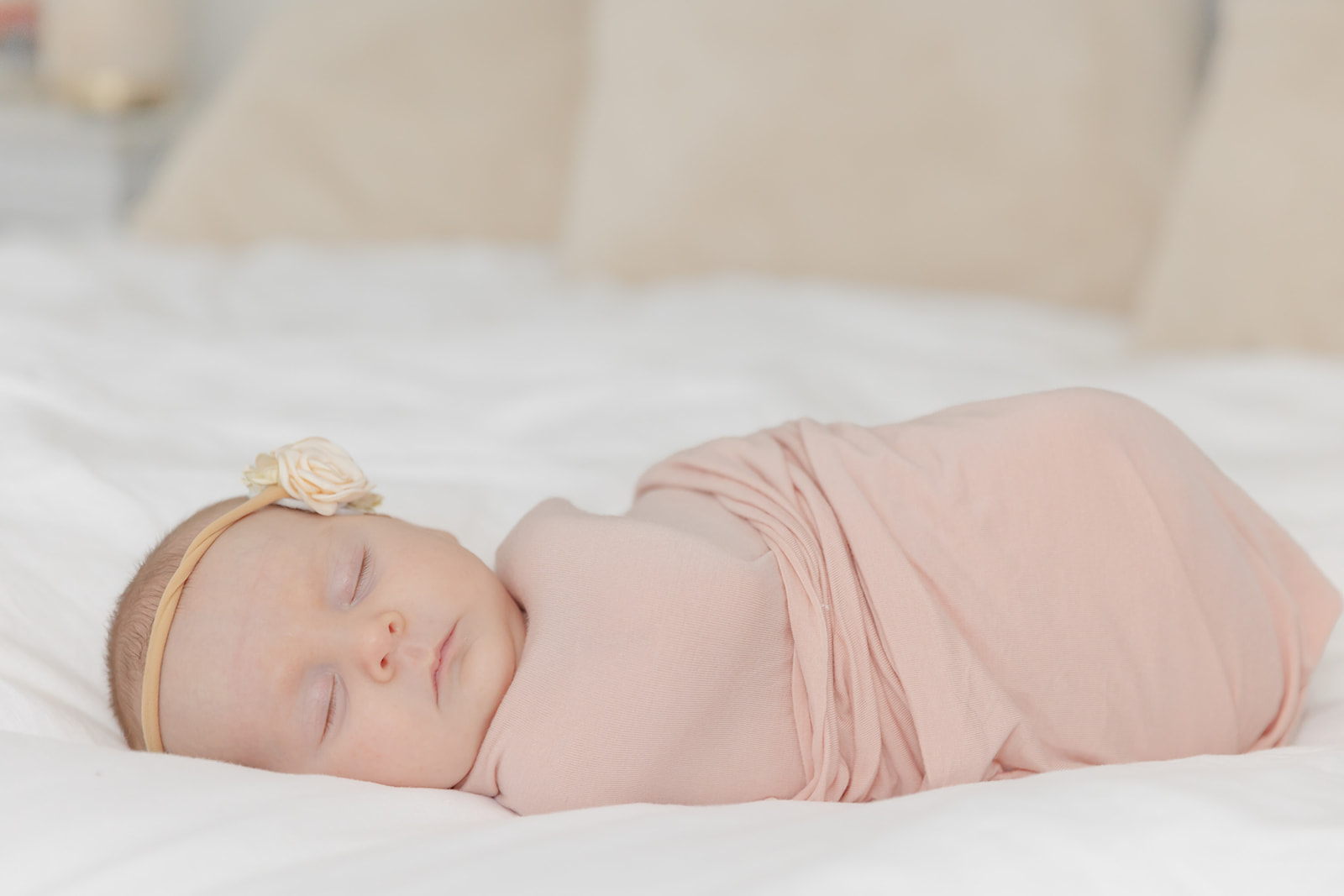 A newborn baby sleeps in a pink swaddle on a white bed thanks to Nightingale Night Nurses