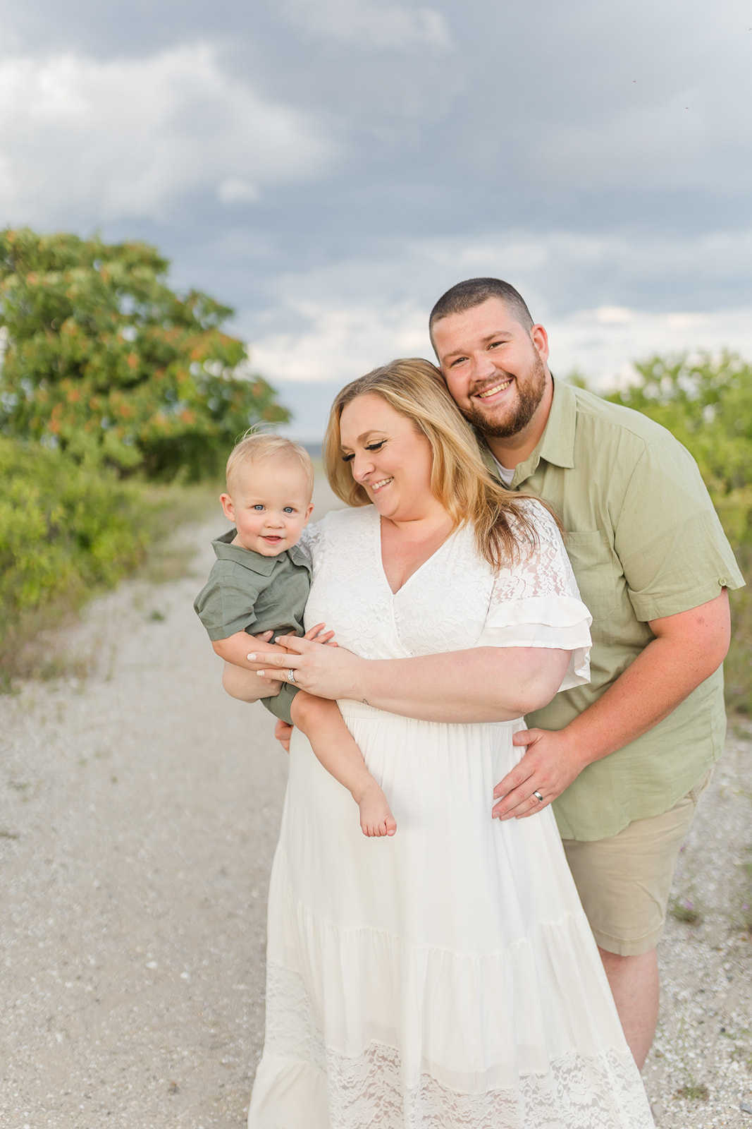 A mother smiles with her husband as they stand on a beach with their toddler son after visiting an OBGYN Fairfield County