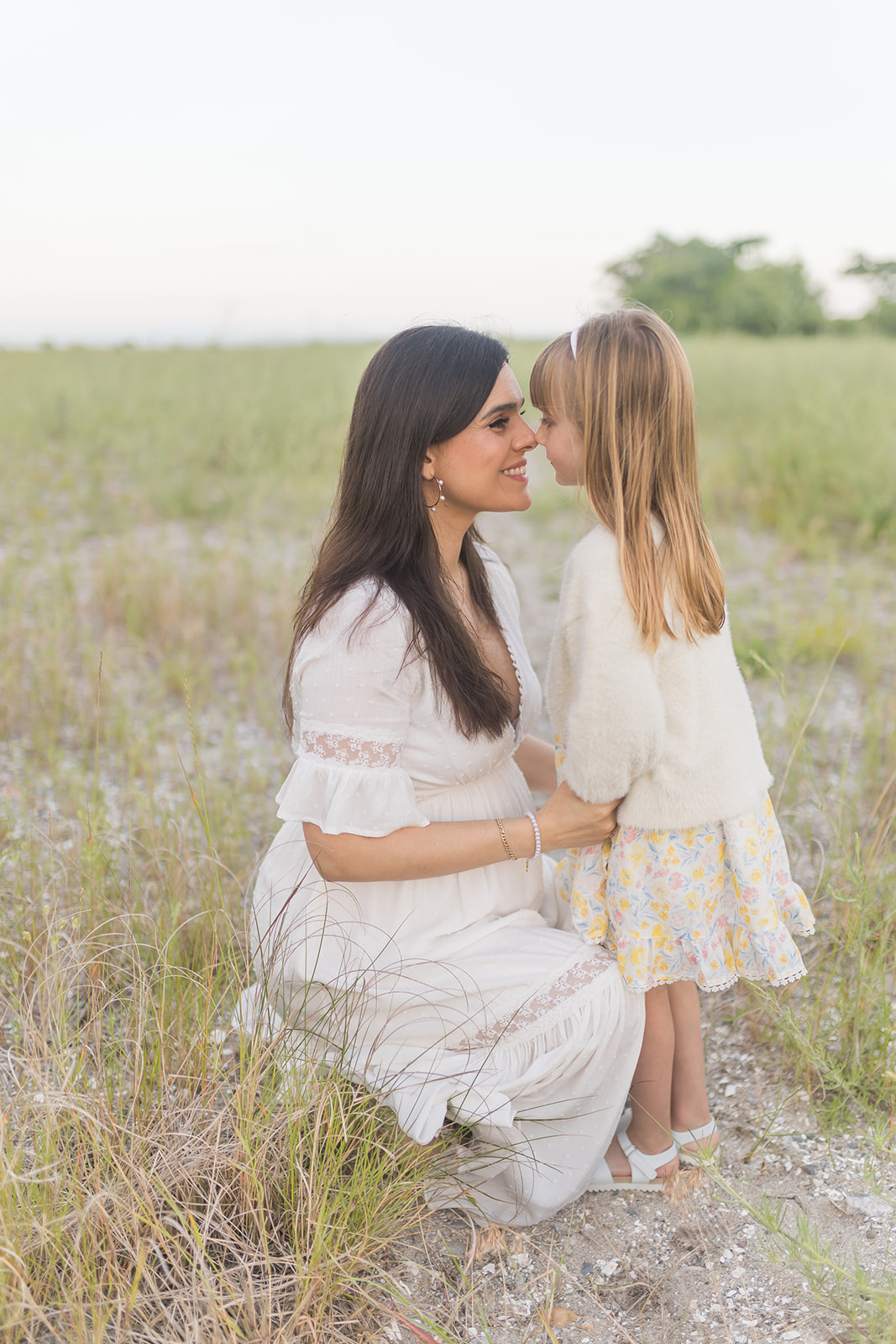 A pregnant mother kneels in a field touching noses with her young daughter