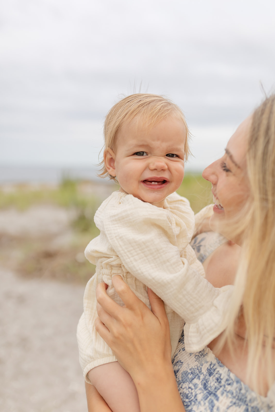 A toddler girl makes a face while sitting in mom's arms on a beach before visiting Playgrounds in Fairfield CT