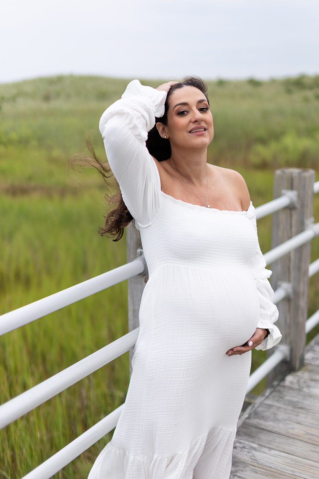 A mother to be brushes her hair back on a windy boardwalk with a hand under her bump before visiting Yale Labor and Delivery
