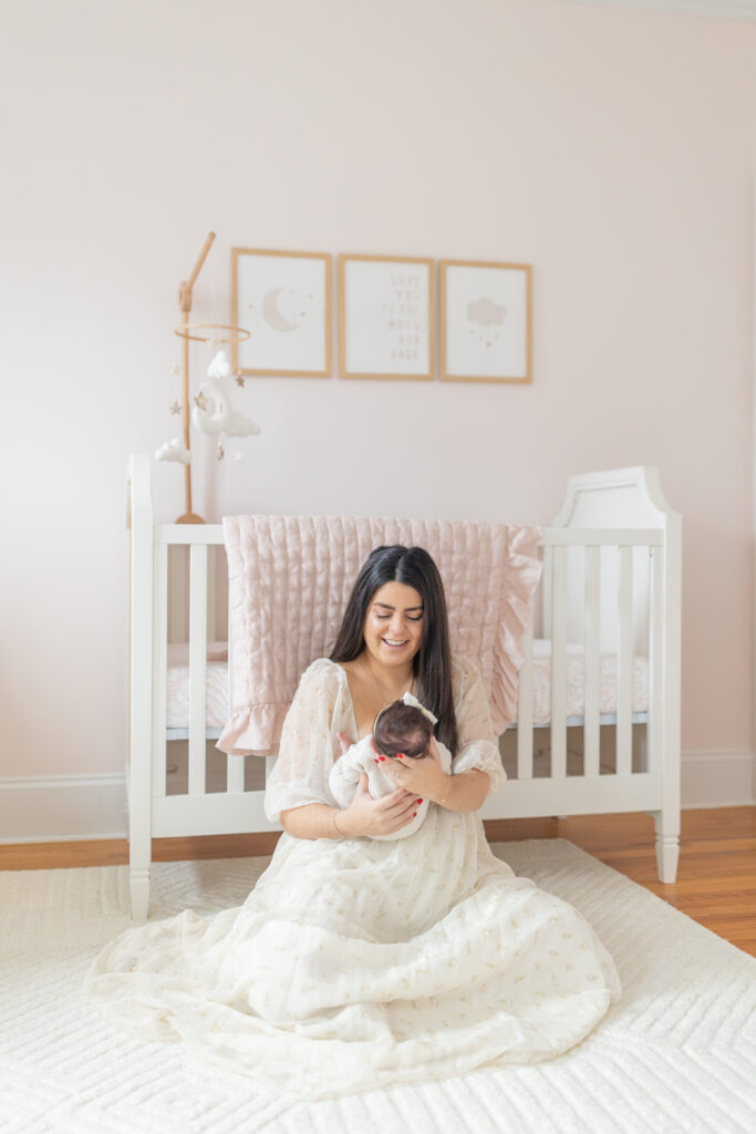 mother smiling at her newborn in front of a white crib in wilton connecticut
