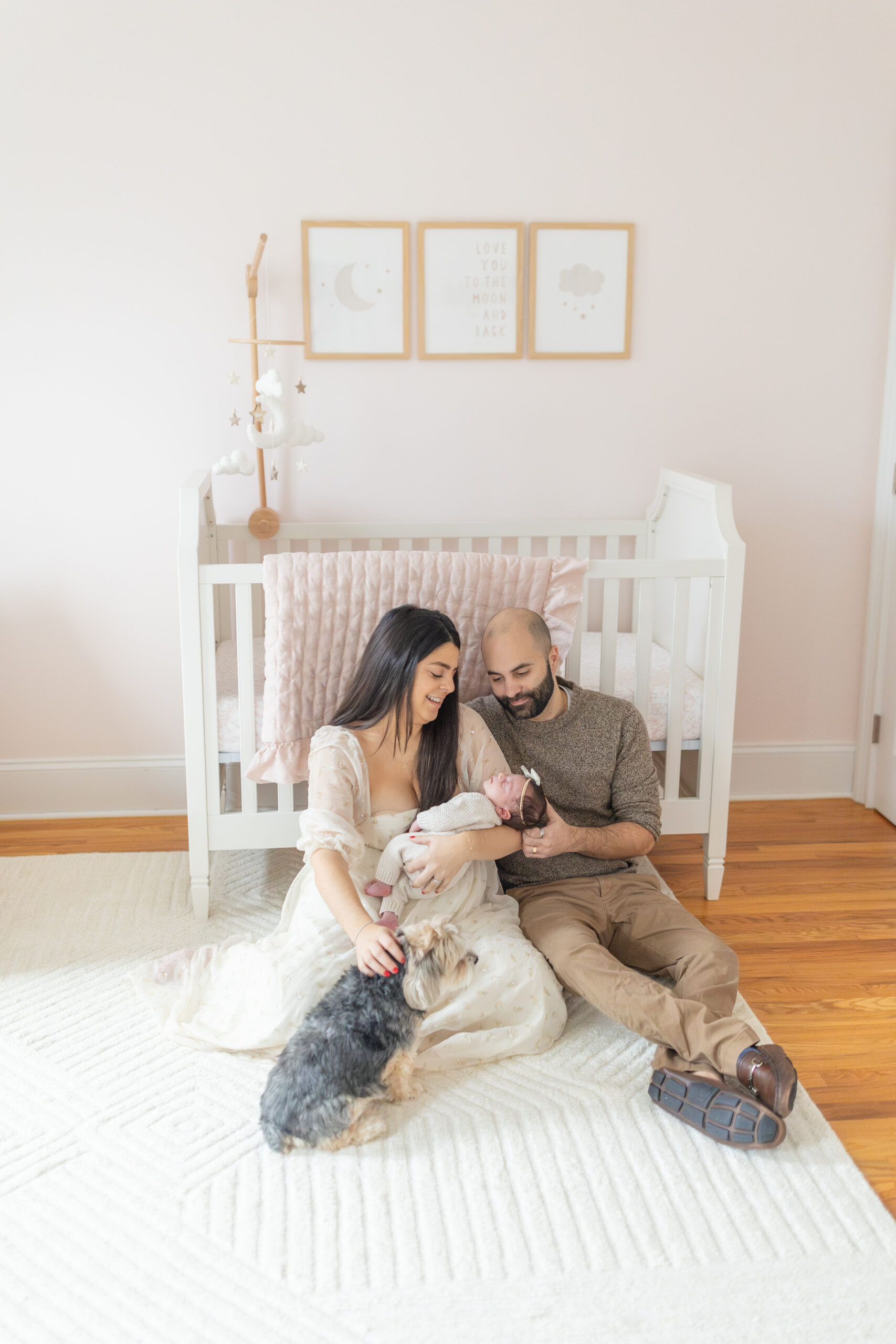 family of three with a newborn and their dog sitting in their nursery in wilton connecticut