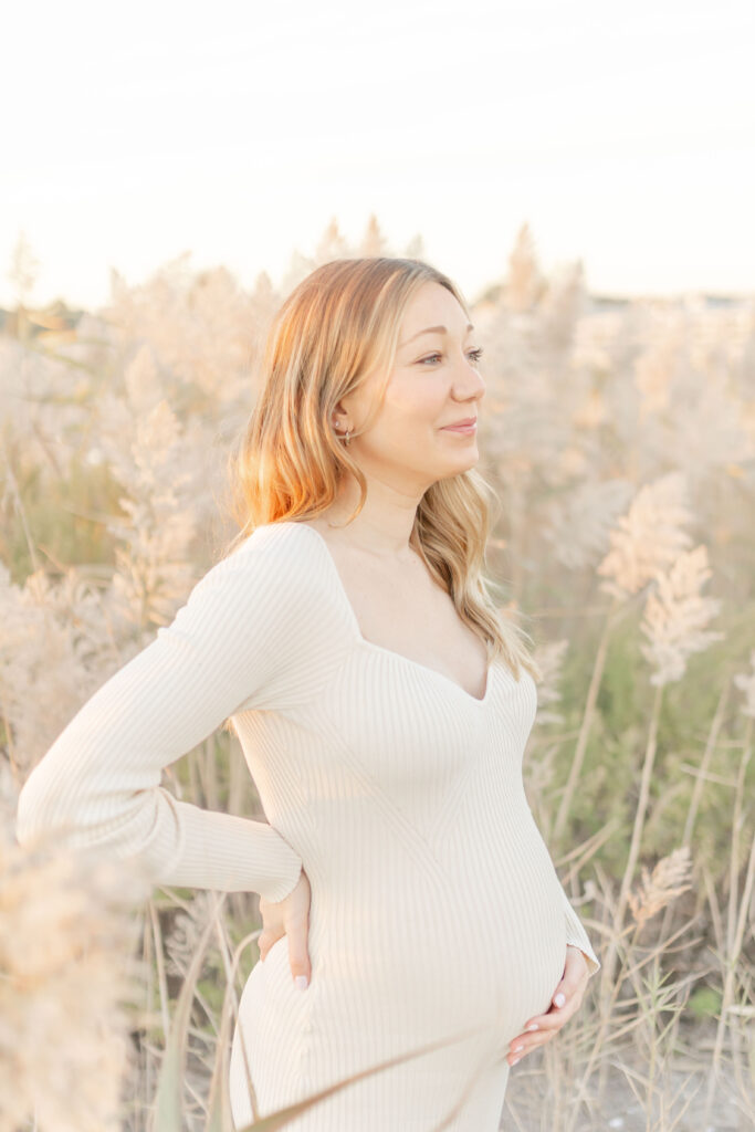 women in maternity dress in winter at the beach surrounded by tall beach grass